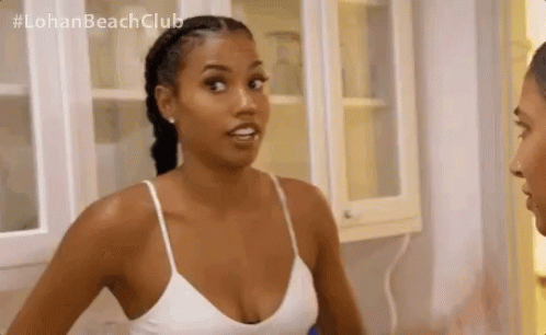 A Woman In A White Tank Top Is Standing Next To A Man In A Kitchen And Talking To Him . GIF