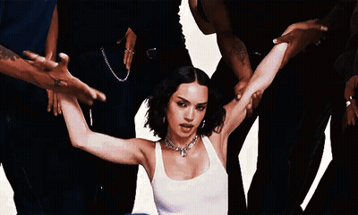 A Woman In A White Tank Top Is Surrounded By A Group Of People . GIF