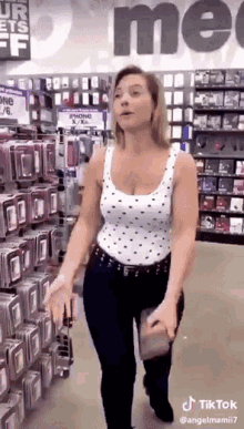 A Woman In A White Tank Top Is Walking Through A Store Holding A Cell Phone Case . GIF