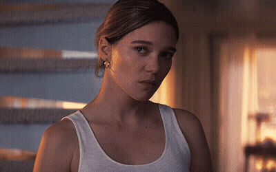 A Woman In A White Tank Top Looks At The Camera With A Serious Look On Her Face GIF