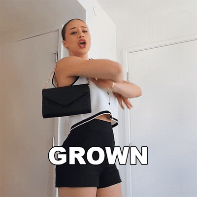 A Woman In A White Top And Black Shorts Is Standing In Front Of A Door With The Word Grown On The Bottom GIF