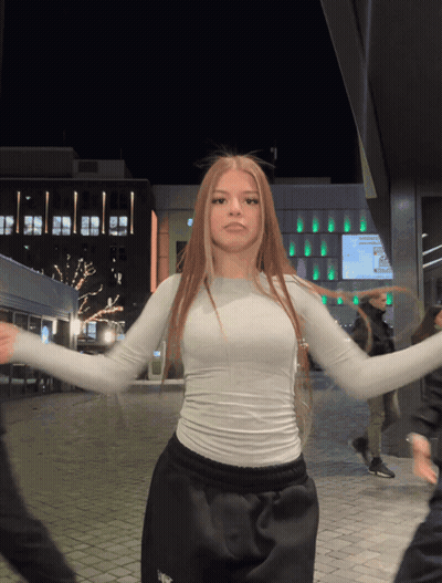 A Woman In A White Top Is Dancing In Front Of A Building GIF