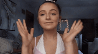 A Woman In A White Top Is Making A Face With Her Hands Outstretched GIF