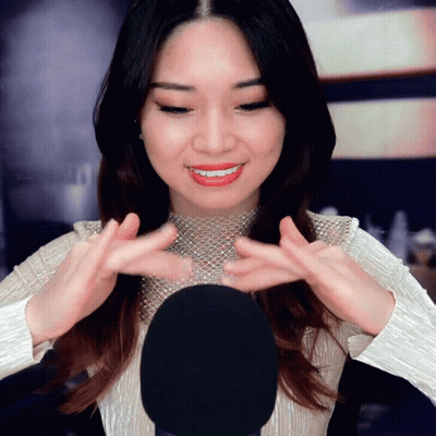 A Woman In A White Top Is Smiling And Holding Her Hands Up In Front Of A Microphone GIF