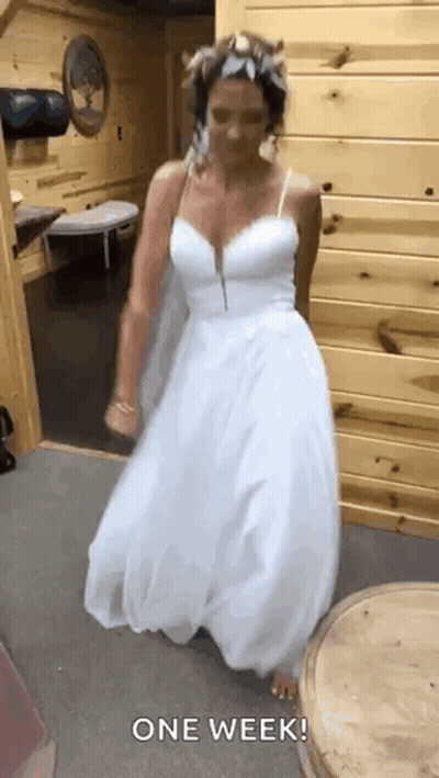 A Woman In A White Wedding Dress Is Dancing In A Room With A Wooden Wall . GIF