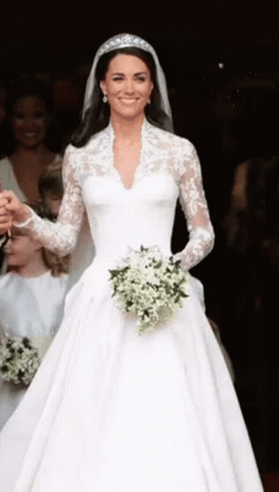 A Woman In A White Wedding Dress Is Holding A Bouquet Of White Flowers . GIF