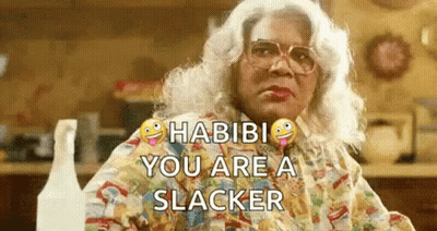 A Woman In A Wig And Glasses Is Sitting At A Table With A Spray Bottle In Front Of Her . GIF