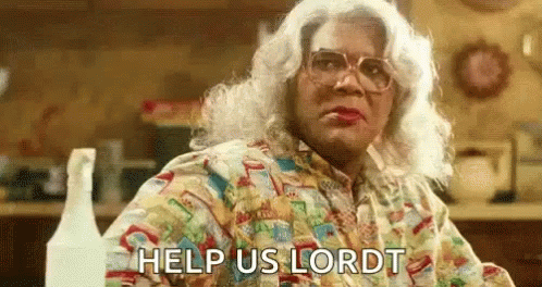 A Woman In A Wig And Glasses Is Sitting At A Table With The Words `` Help Us Lord '' Written On Her Face . GIF