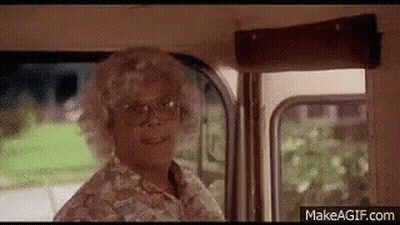 A Woman In A Wig And Glasses Is Standing In A Bus . GIF