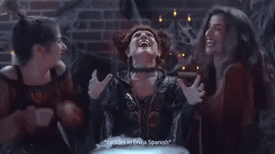 A Woman In A Witch Costume Says " Cackles In Bruja Spanish " While Two Other Women Look On GIF
