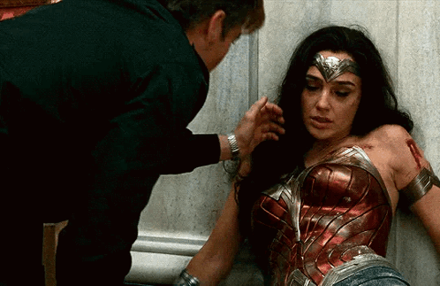 A Woman In A Wonder Woman Costume Is Laying On The Ground While A Man Holds Her Arm . GIF
