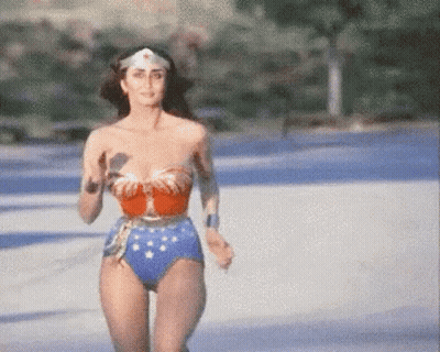 A Woman In A Wonder Woman Costume Is Running Across A Road . GIF