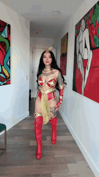 A Woman In A Wonder Woman Costume Is Standing In A Hallway Holding A Sword . GIF