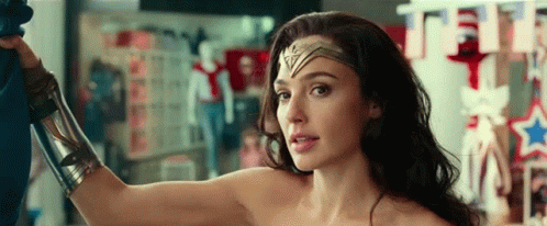 A Woman In A Wonder Woman Costume Is Standing In A Room With Her Arm Up . GIF