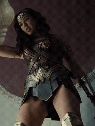 A Woman In A Wonder Woman Costume Is Standing In Front Of A Purple Wall GIF