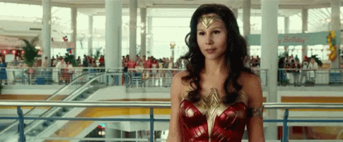 A Woman In A Wonder Woman Costume Is Standing On A Balcony In A Shopping Mall . GIF