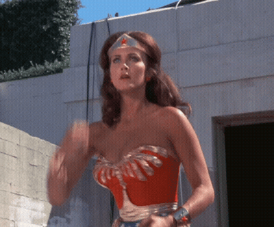 A Woman In A Wonder Woman Costume Is Waving GIF