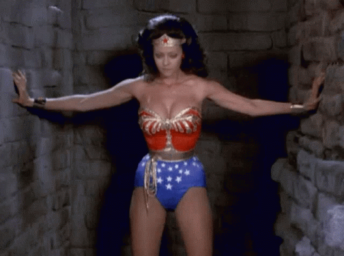 A Woman In A Wonder Woman Outfit Is Standing In A Dark Room GIF