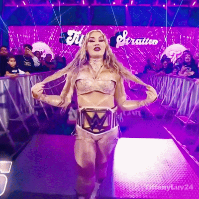 A Woman In A Wrestling Outfit Is Walking Down A Purple Aisle With The Word Stratton Behind Her GIF
