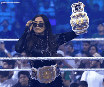 A Woman In A Wrestling Ring Holding A Championship Belt And Wearing Sunglasses GIF