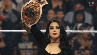 A Woman In A Wrestling Ring Holds Up A Gold Wrestling Championship Belt GIF