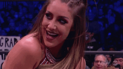 A Woman In A Wrestling Ring Is Smiling In Front Of A Crowd Of People . GIF