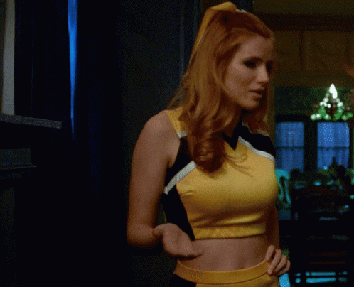 A Woman In A Yellow And Black Cheerleader Outfit Stands With Her Hand On Her Hip GIF