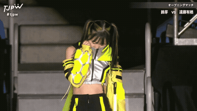 A Woman In A Yellow And Black Outfit With The Letters Tjpw On The Top GIF