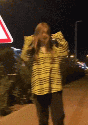 A Woman In A Yellow And Black Striped Shirt Is Standing In Front Of A Red And White Sign GIF