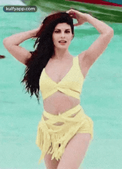 A Woman In A Yellow Bikini Is Standing In A Pool Of Water . GIF
