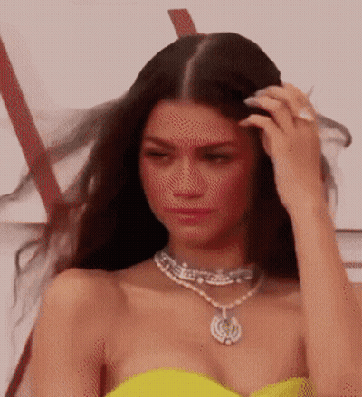 A Woman In A Yellow Dress And Necklace Is Touching Her Hair . GIF