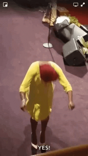 A Woman In A Yellow Dress And Red Hat Is Dancing In Front Of A Microphone And Says Yes GIF