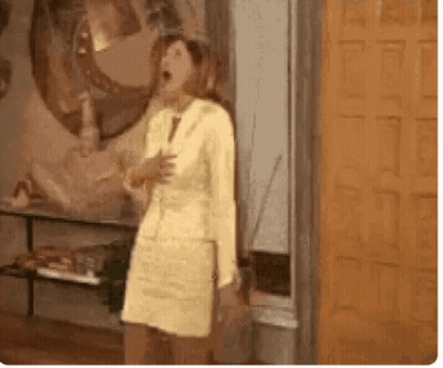 A Woman In A Yellow Dress And Suit Is Standing In Front Of A Door . GIF
