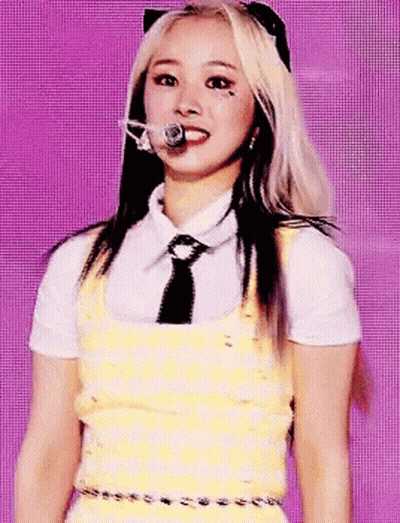 A Woman In A Yellow Dress And Tie Is Standing In Front Of A Microphone . GIF