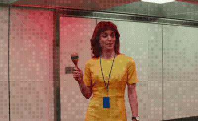 A Woman In A Yellow Dress Is Holding A Maraca In Her Hand GIF