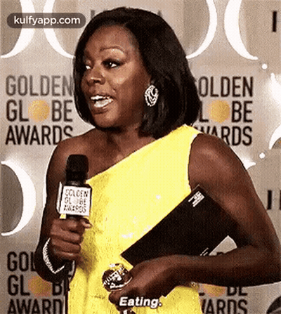 A Woman In A Yellow Dress Is Holding A Microphone And Talking Into It At The Golden Globe Awards . GIF