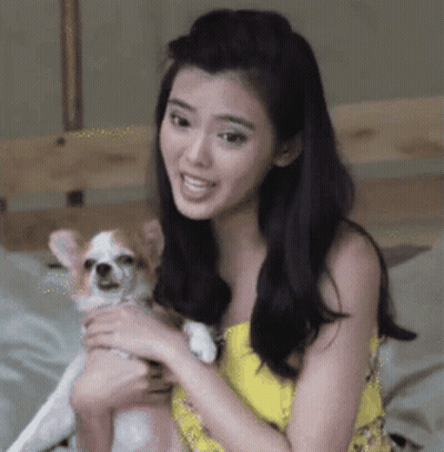 A Woman In A Yellow Dress Is Holding A Small Dog In Her Arms GIF