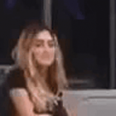 A Woman In A Yellow Dress Is Sitting In Front Of A Window And Talking On A Cell Phone . GIF