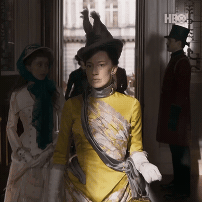 A Woman In A Yellow Dress Is Standing In A Doorway With A Hbo Logo In The Background GIF