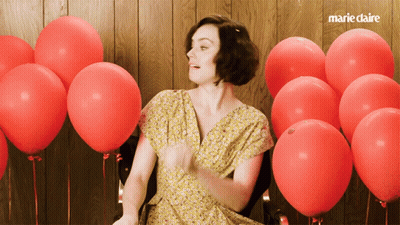 A Woman In A Yellow Dress Is Surrounded By Red Balloons And The Words Marie Claire Are On The Bottom GIF