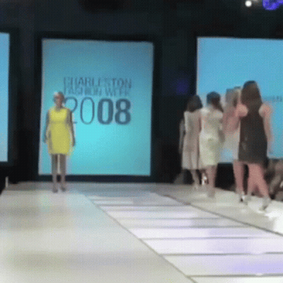 A Woman In A Yellow Dress Is Walking Down A Runway At The Charleston Fashion Week 2008 GIF