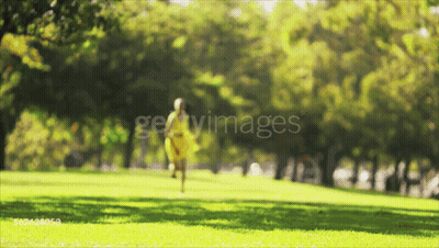 A Woman In A Yellow Dress Is Walking Through A Park GIF