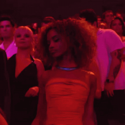 A Woman In A Yellow Dress Stands In A Crowd Of People GIF