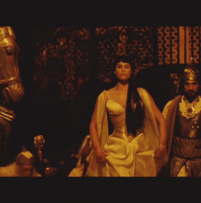 A Woman In A Yellow Dress Stands In Front Of A Man In Armor GIF