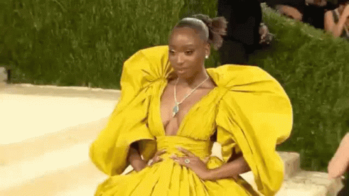 A Woman In A Yellow Dress With A Plunging Neckline And Huge Sleeves Is Sitting On The Ground . GIF