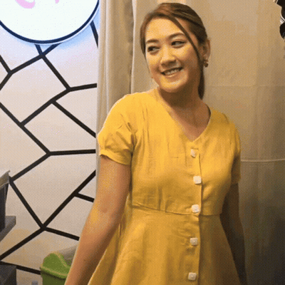 A Woman In A Yellow Dress With White Buttons On The Front GIF