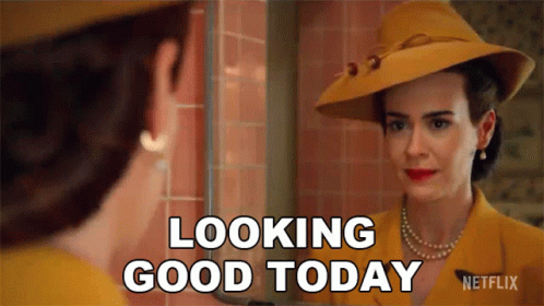 A Woman In A Yellow Hat Is Looking At Herself In A Mirror And Saying Looking Good Today . GIF