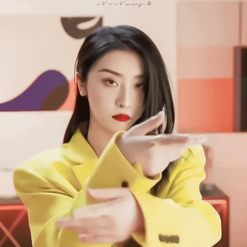 A Woman In A Yellow Jacket Is Making A Gesture With Her Arms GIF