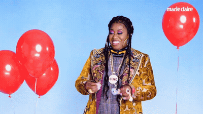 A Woman In A Yellow Jacket Is Surrounded By Red Balloons And Has A Cinc Necklace Around Her Neck GIF