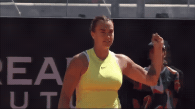 A Woman In A Yellow Nike Tank Top Holds Her Fist Up GIF